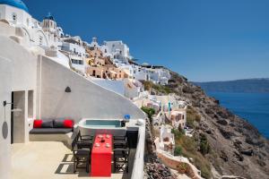 einen Balkon mit Stühlen und einem Pool auf einem Hügel in der Unterkunft Satori Caves by Thireon in Oia
