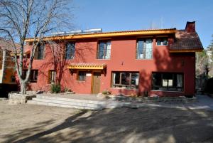 ein rotes Gebäude mit einem Baum davor in der Unterkunft Casa Rural Mansion Alejandra con piscina y jacuzzi in Collado Mediano