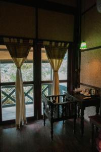 um quarto com uma mesa e duas janelas com cortinas em Nong Kiau Riverside em Nongkhiaw