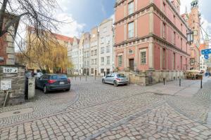 two cars are parked on a cobblestone street with buildings at Apartments Old Town Ogarna 107 by Renters in Gdańsk