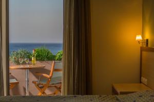 a room with a table and a balcony with the ocean at Alianthos Beach Hotel in Plakias