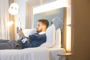 a man laying on a bed holding a cell phone at Novotel RJ Porto Atlantico in Rio de Janeiro