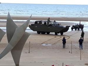 サン・ローラン・シュル・メールにあるAppartement OMAHA BEACHの浜辺にボートがあり、周りに人々が立っている +2枚の写真