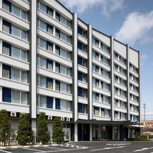 een groot wit gebouw met bomen ervoor bij Smile Hotel Sendai Tagajyo in Tagajo