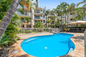 a swimming pool in front of a building with palm trees at The Burlington Holiday Apartments in Maroochydore