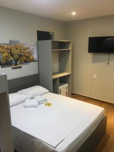 a bedroom with a white bed with a flat screen tv at Mirante dos Anjos Suítes in Arraial do Cabo