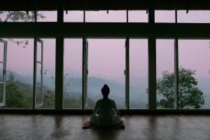 a woman sitting in a yoga pose in front of a window at SpiceTree Rajakumari in Munnar