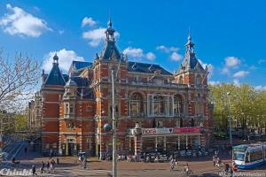 un grand bâtiment en briques rouges avec des personnes devant lui dans l'établissement Leidse Square 5 star Luxury Apartment, à Amsterdam