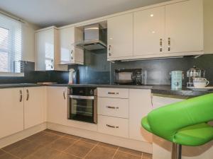 una cucina con armadi bianchi e una sedia verde di Rowan Cottage a St Bees