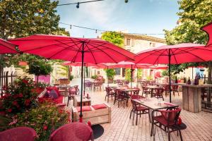 eine Terrasse mit Tischen, Stühlen und roten Sonnenschirmen in der Unterkunft Village Castigno - Wine Hotel & Resort in Assignan