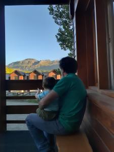 un hombre sentado en un porche sosteniendo a un niño en Departamentos Mirador del Maipú en San Martín de los Andes