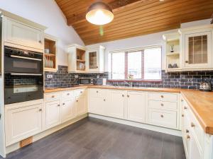 a kitchen with white cabinets and a wooden ceiling at Frog Meadow Barn in Biddulph