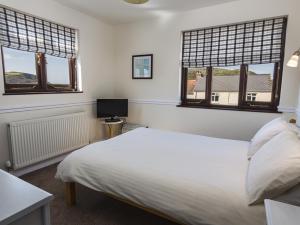 a bedroom with a white bed and two windows at 4 Armada House in Hope Cove