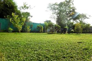a field of green grass with a fence and trees at Hotel Nimjaya in Udawalawe