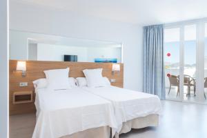 a white bedroom with a large white bed and a table at Aparthotel Ses Fotges in Playa de Muro
