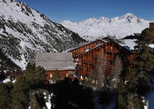 un grand bâtiment avec des montagnes enneigées en arrière-plan dans l'établissement Résidence Les Arolles by Les Etincelles, à Arc 2000