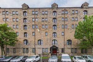 a large brick building with cars parked in a parking lot at Stunning 2 Bed Merchant City Apartment with Residents Parking (Bell 2) in Glasgow