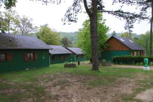 two green buildings with a tree in the yard at Camping de la Pelouse in Jaulny