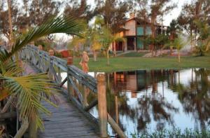 un pont en bois sur un étang avec une maison en arrière-plan dans l'établissement Casa condomínio lagoa cortada, à Balneário Gaivotas