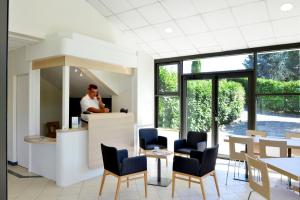 a man standing at a counter in a restaurant with chairs and tables at The Originals City, Clos de l'Orgerie ,Château Gonthier in Château-Gontier