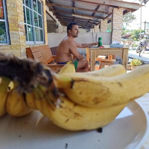 un hombre sentado en una mesa con un montón de plátanos en DAOH'S Rooms & Scooters, en Tanjung Rhu