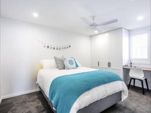 a white bedroom with a bed and a ceiling fan at Kirra Waves in Gold Coast