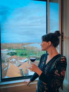 a woman holding a glass of wine looking out a window at Chalet Santa Iria in Santarém