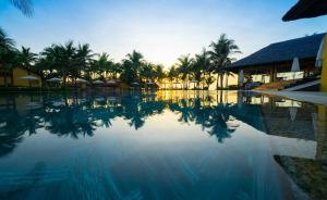 a large swimming pool with palm trees in the background at Pandanus Resort in Mui Ne