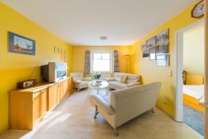 Il comprend un salon avec des murs jaunes, un canapé et une télévision. dans l'établissement DER SÜDSCHWEDE ... Dein Gästehaus mitten in Zingst und nah zum Strand, à Zingst
