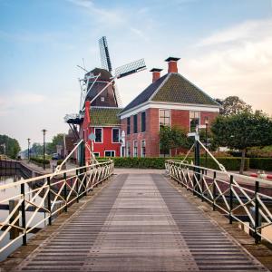 a bridge over a river with a building and windmills at Molen Hunsingo in Onderdendam