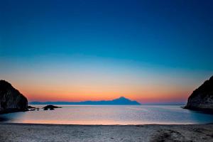 a sunset over a beach with a mountain in the background at Kissos Apartments in Vourvourou