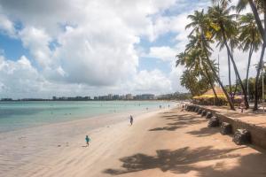 a beach with people in the water and palm trees at Hotel Ciribaí in Maceió