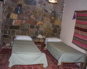 two beds in a room with a stone wall at Hostal de Altura in Tilcara
