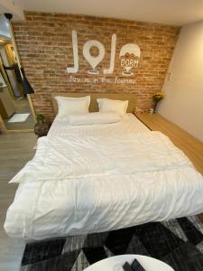 Cette chambre comprend un grand lit blanc et un mur en briques. dans l'établissement jojoroom, à Hô-Chi-Minh-Ville