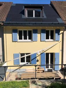 Casa amarilla con ventanas con persianas azules y porche en B&B Tomsi, en Pratteln