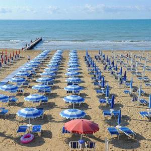 un mucchio di sedie blu e ombrelloni su una spiaggia di Hotel Mirage a Lido di Jesolo