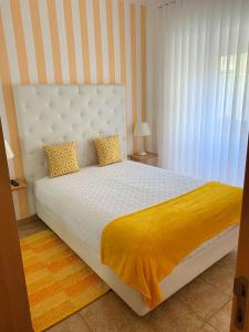 1 dormitorio con 1 cama blanca con manta amarilla en Duarte Houses T2 - com vista mar, en Nazaré