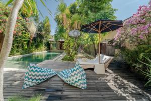 an outdoor deck with an umbrella and chairs next to a pool at Villa Saffira in Seminyak
