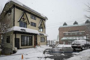 eine schneebedeckte Straße mit einem Gebäude und einem Auto in der Unterkunft Iroha Nozawa in Nozawa Onsen