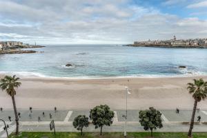 a beach with people walking on the sand and the ocean at APARTAMENTO EN PRIMERA LINEA DE PLAYA RiAZOR in A Coruña