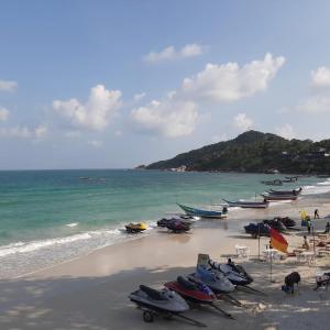 a beach with boats and chairs and the ocean at Sunrise Resort- Koh Phangan - SHA Extra Plus in Haad Rin
