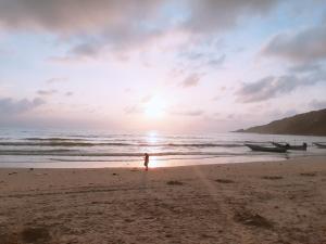 a person standing on a beach with a boat at Sunrise Resort- Koh Phangan - SHA Extra Plus in Haad Rin