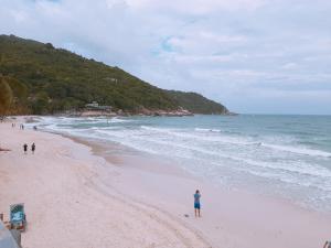 a person standing on a beach next to the ocean at Sunrise Resort- Koh Phangan - SHA Extra Plus in Haad Rin