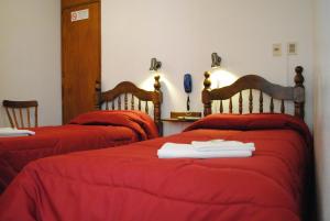 2 Betten in einem Zimmer mit roter Bettwäsche und Handtüchern darauf in der Unterkunft Hotel Romi in Colonia del Sacramento