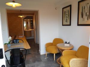 a room with yellow chairs and tables and a hallway at Le P'tit gousset, à 100 m de la mer in Donville-les-Bains