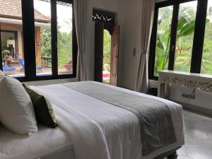 a bedroom with a large white bed with windows at Puri Kasih Gottlieb in Ubud