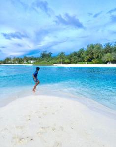 Ein Mann steht am Strand im Wasser in der Unterkunft Ocean Way Guraidhoo in Guraidhoo