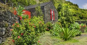 uma casa de pedra com uma janela vermelha e algumas plantas em Casas de Incensos - TER -TA em Pontas Negras