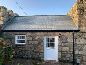 a stone cottage with a white door and two windows at The Studio @ The Old Vicarage in Pendeen