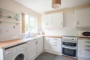 una cocina con armarios blancos, lavadora y fregadero en Glasgow's Cosy Family Home Near SECC Hydro en Glasgow